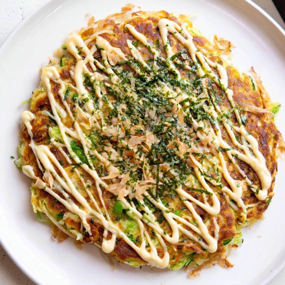 Golden-brown Japanese Okonomiyaki pancake topped with savory sauce, creamy mayo, and dancing bonito flakes.