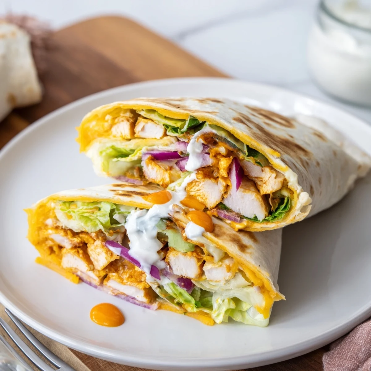 A freshly assembled Buffalo Ranch Chicken Wrap showcases vibrant romaine lettuce, shredded cheddar, and juicy buffalo chicken nestled in a warm flour tortilla. 