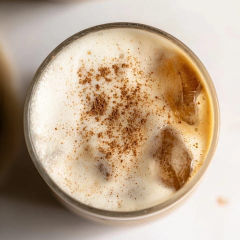 In a tall glass, chilled chai tea sits beneath a thick, creamy cold foam topping, evoking the warmth of aromatic spices on a hot summer day.