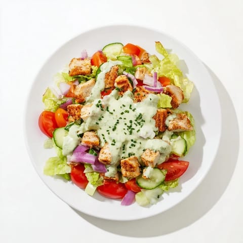 Fresh avocado ranch chicken salad served in a bowl with cherry tomatoes, cucumbers, and vibrant herbs.