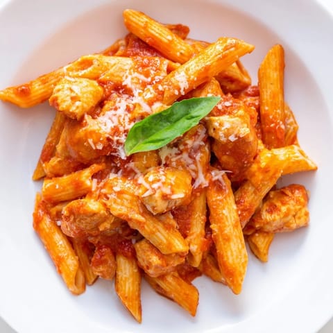 Steam rises from a bowl of Tomato Basil Chicken Pasta, with tender chicken pieces nestled in a rich red sauce garnished with fresh basil.