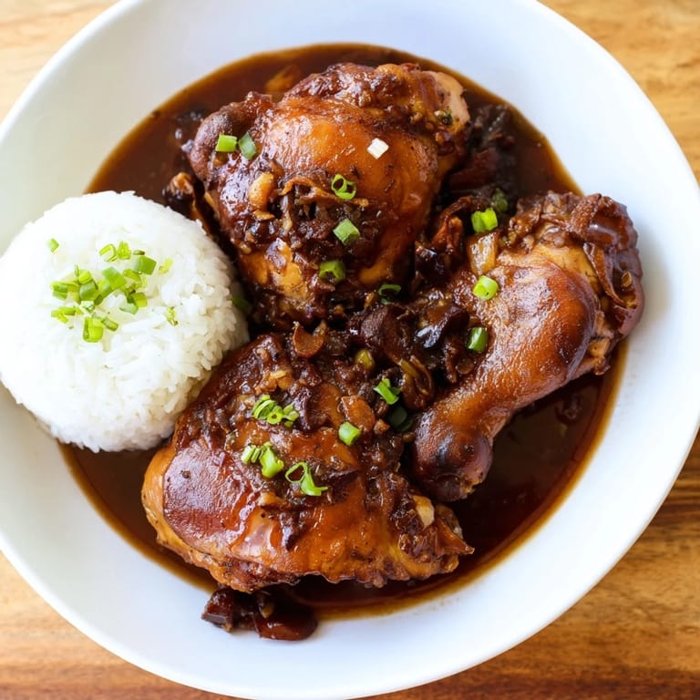 Steaming plate of Filipino Chicken Adobo with rice, garnished and ready for a delicious dinner.